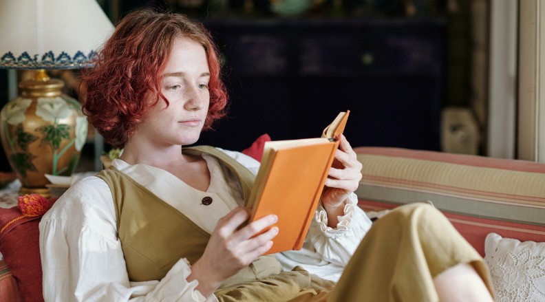 Puber met rode krullen leest boek op bank